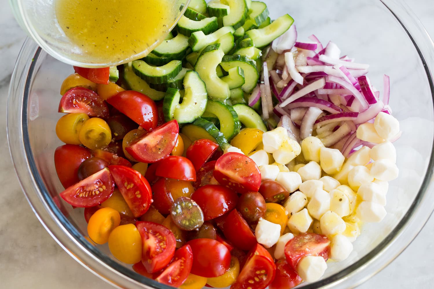 Panzanella Salad Panzanella salad ingredients in a mixing bowl with dressing being poured over.