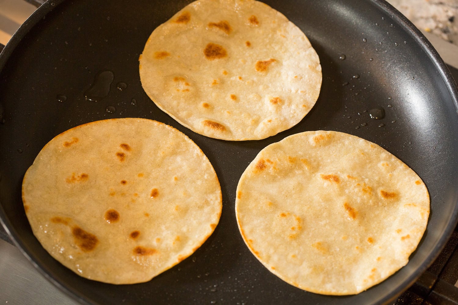 Huevos Rancheros Heating corn tortillas in oil in dark non-stick skillet.