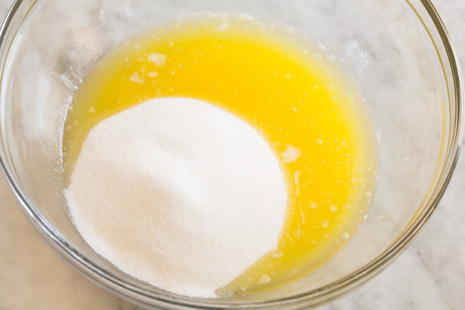Brownie Bites Melted butter with white sugar in a glass mixing bowl.