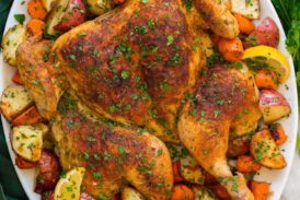 Spatchcock chicken with potatoes and carrots shown on a large oval white serving platter with lemons.