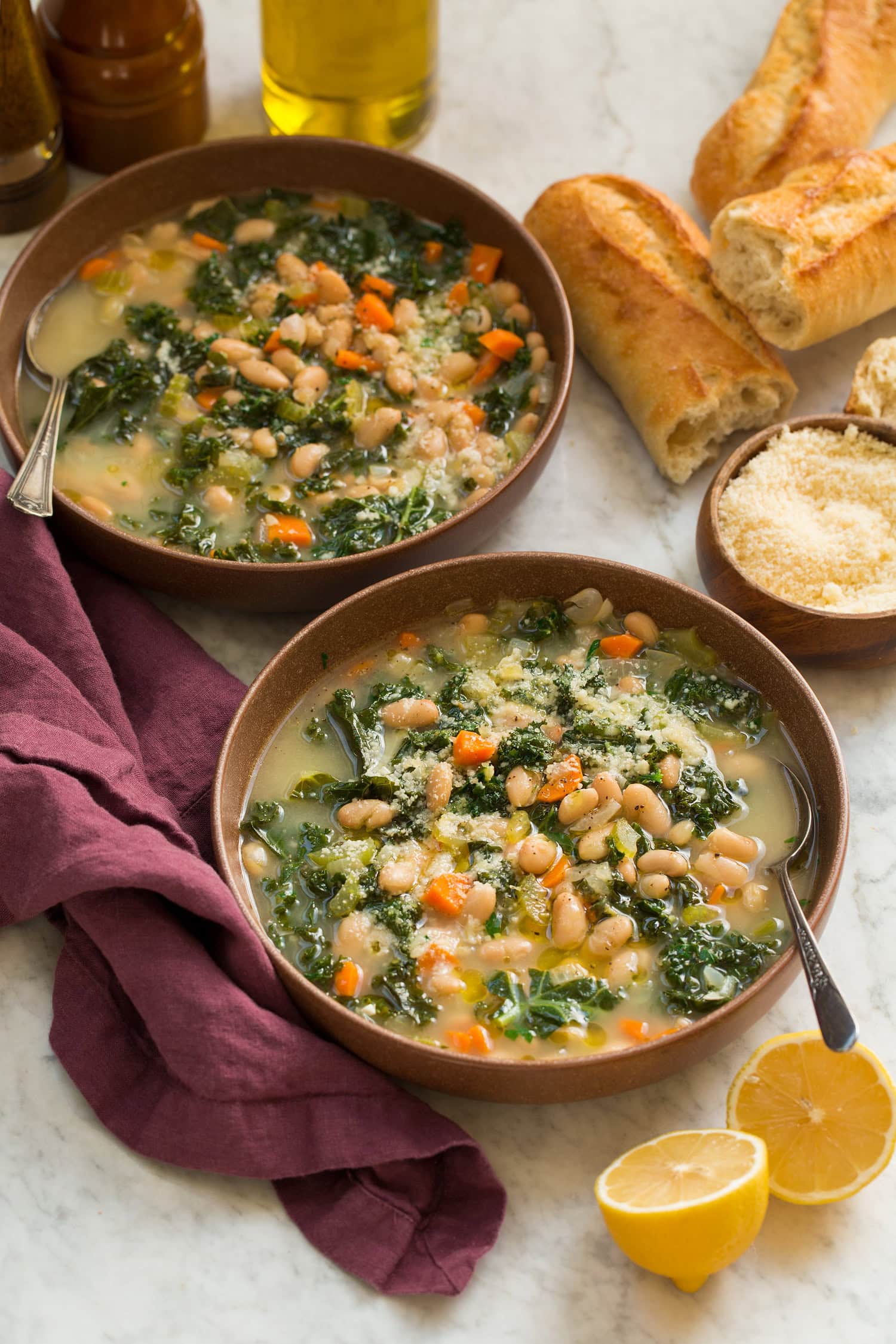 Two bowls of white bean kale soup on a purple cloth.