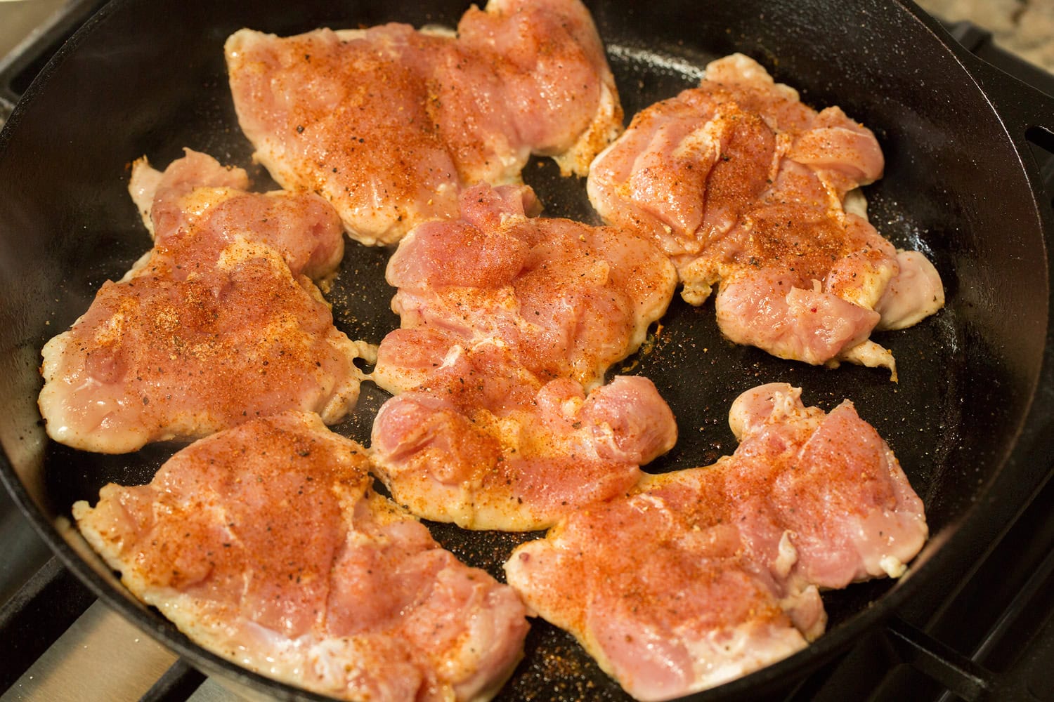 Apple Chicken Raw chicken thighs searing in a cast iron pan.
