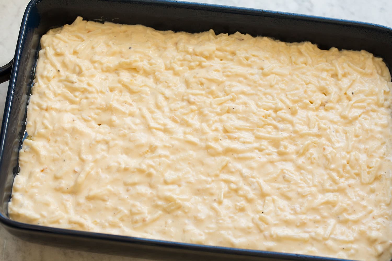 Sauce coated hash browns spread out even in a baking dish.