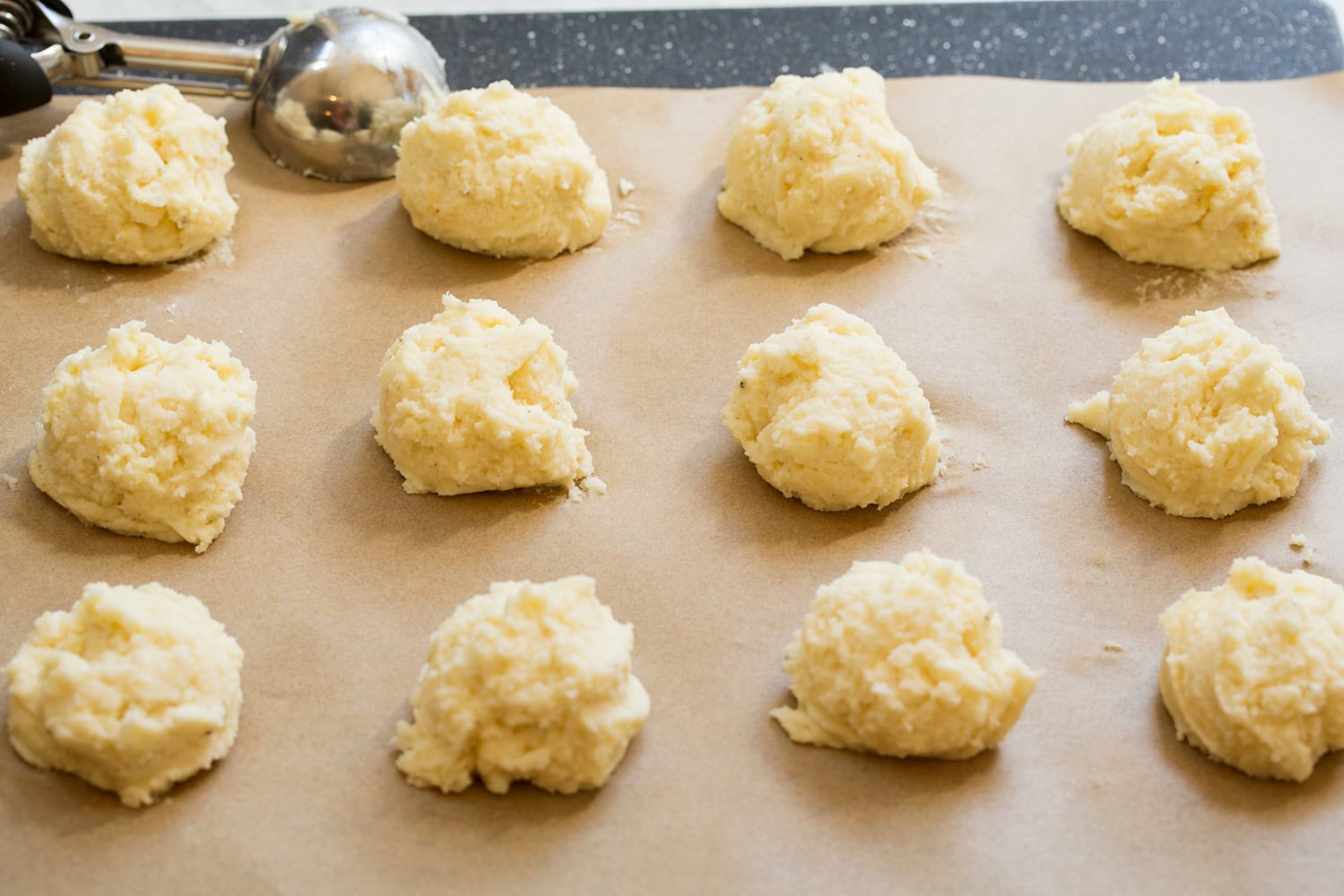 Scoopfuls of mashed potato cake mixture on parchment paper.