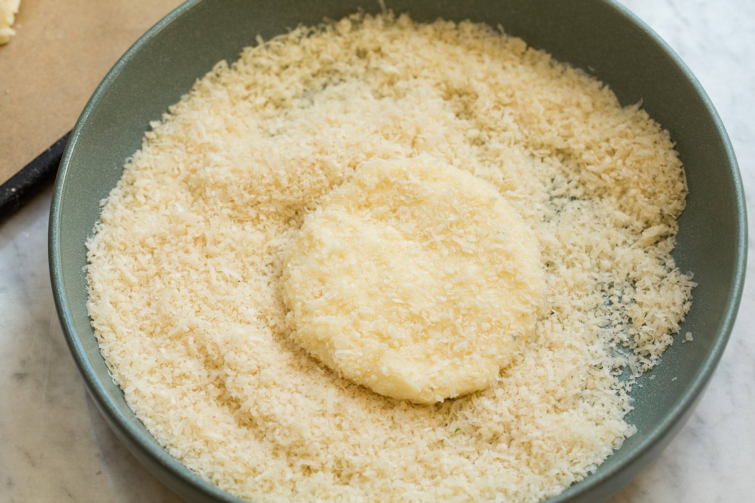 Potato cake pattie being coated in panko bread crumbs and parmesan.