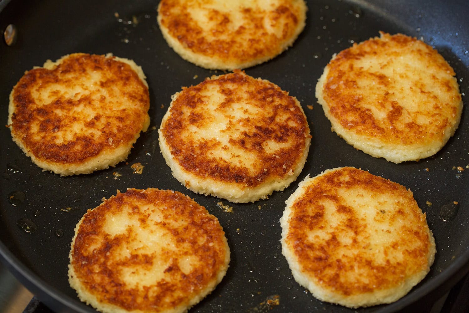 Mashed potato cakes shown after being cooked in a skillet and browned.