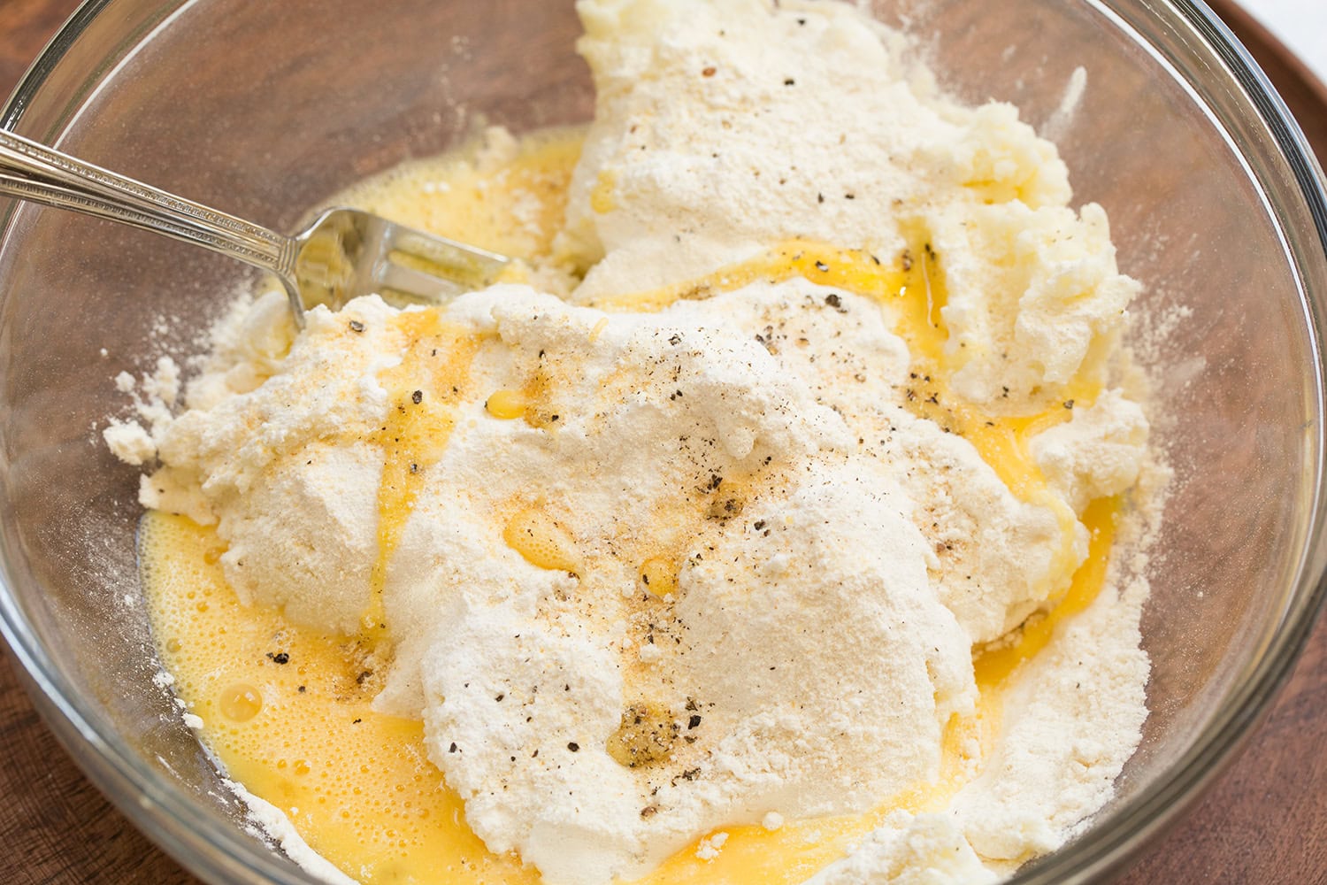 Potato cake mixture with flour and eggs shown before mixing in a glass mixing bowl.