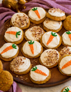 Carrot cake cookies on a wooden platter shown with a purple cloth and bunny decorations to the side.