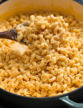 Close up photo of mac and cheese scooped out on a wooden spoon. Shows thick creamy texture of sauce and stringy cheese.
