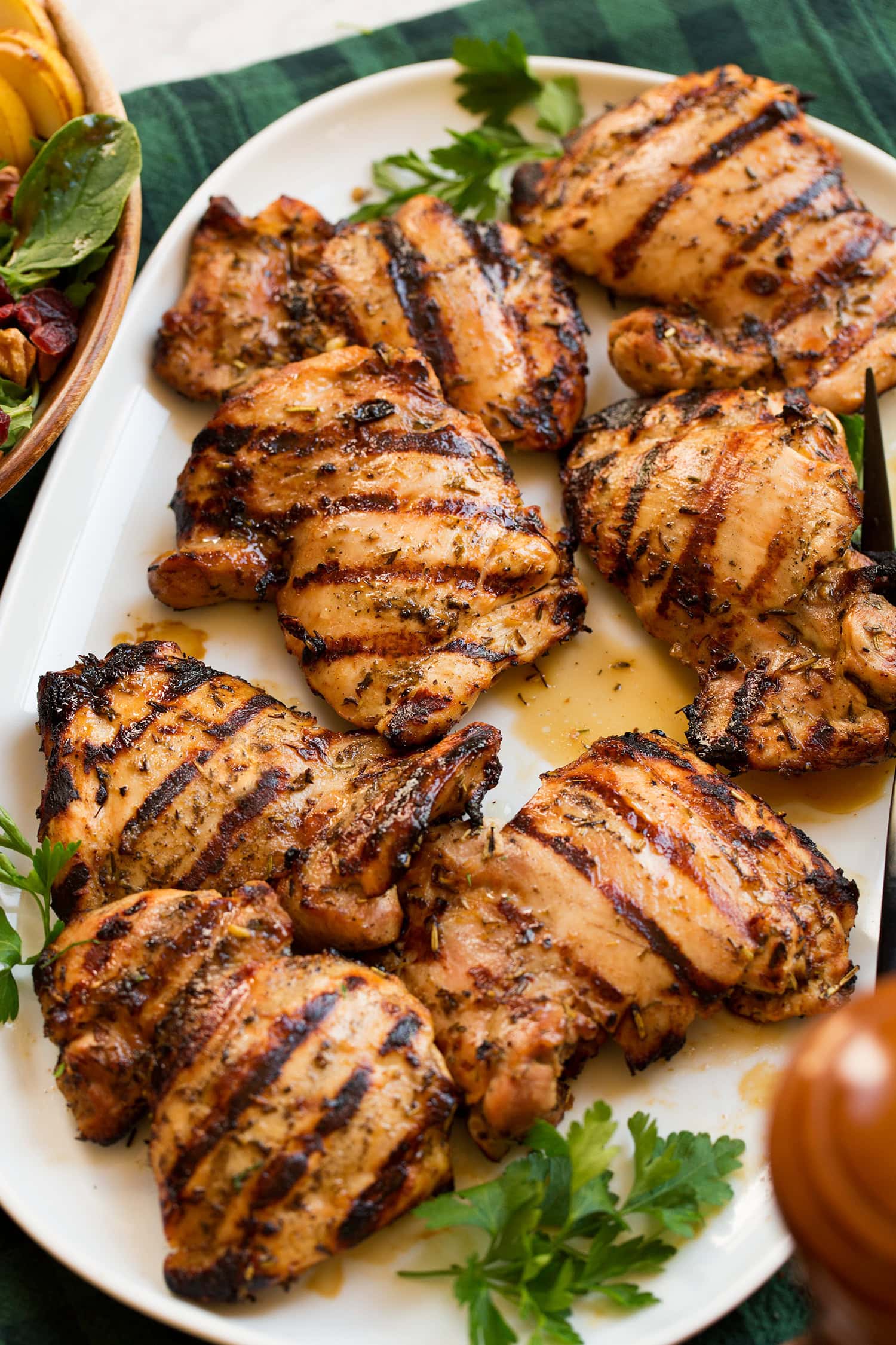 Grilled chicken thighs with pretty black grill marks shown in a single layer on a platter with parsley to the side for garnish.