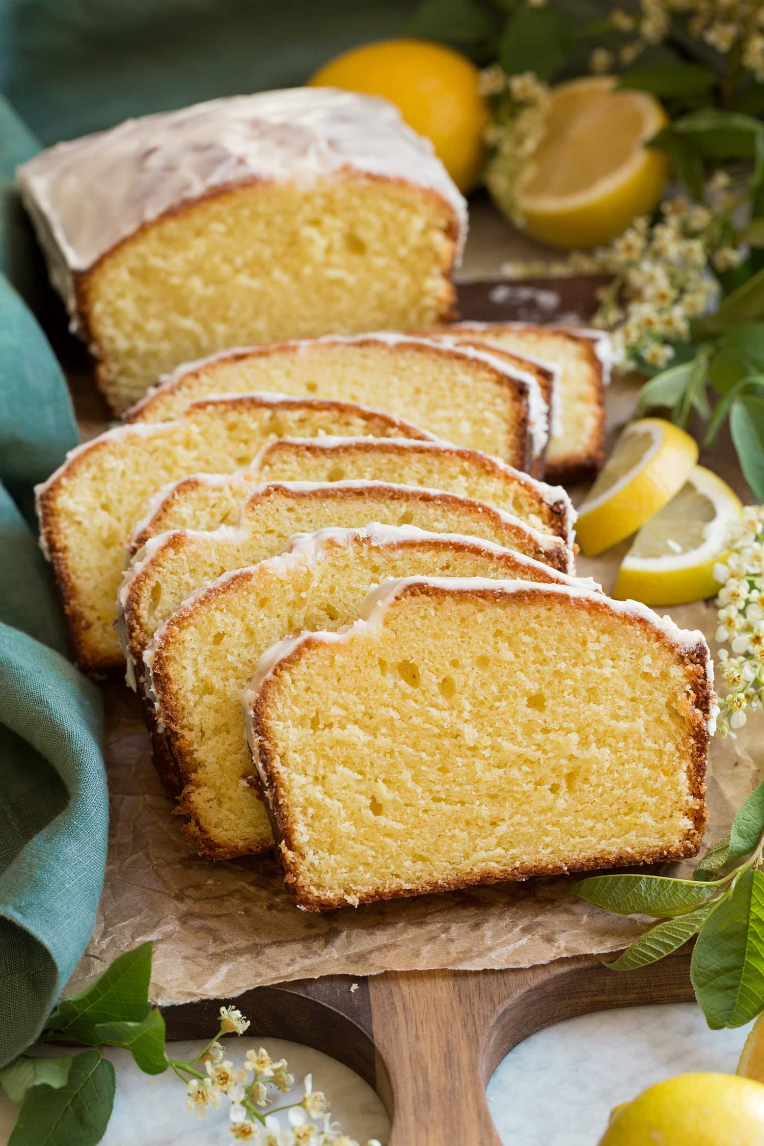 Lemon Pound Cake Loaf of lemon pound cake with a vanilla glaze on top. Loaf is cut into slices with 1/3 of the loaf left whole. It's placed on a wooden serving tray with tan parchment paper atop it.