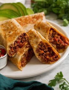 Easy homemade ground beef burritos shown aligned on a platter and cut into halves to show filling.