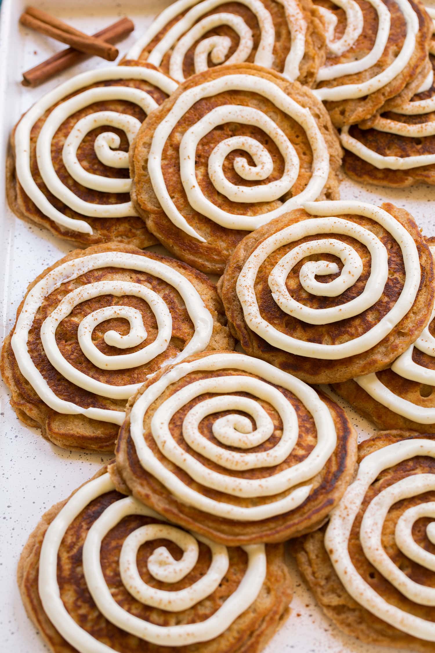 Cinnamon Roll Pancakes Homemade cinnamon pancakes with a cream cheese icing in a swirl piped over the top of the pancakes.